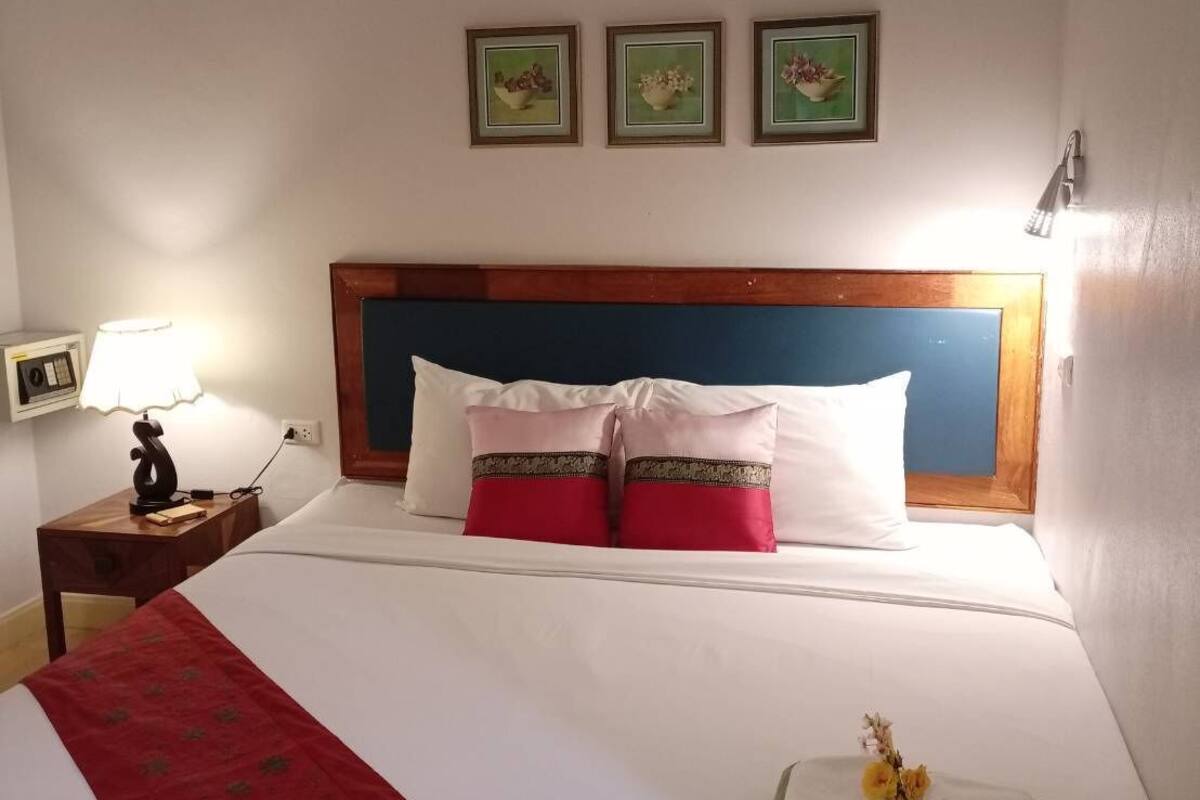 A neatly made bed with white and red bedding, a red decorative runner, and a set of green towels.
