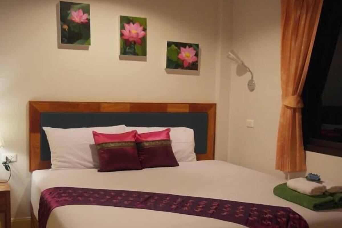A neatly made bed with a wooden headboard, a bedside lamp, and three wall-mounted flower paintings.