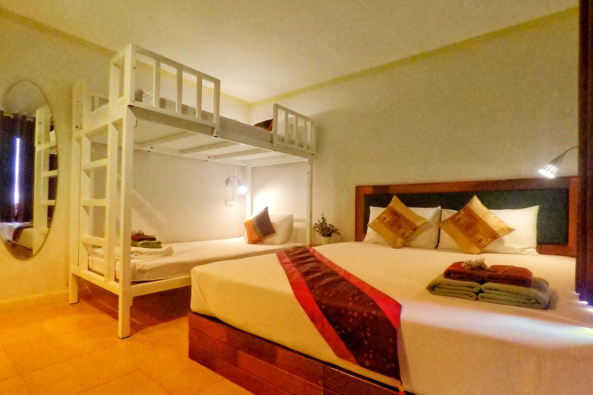 A hotel room with a bunk bed, a single bed, and a nightstand with a lamp.