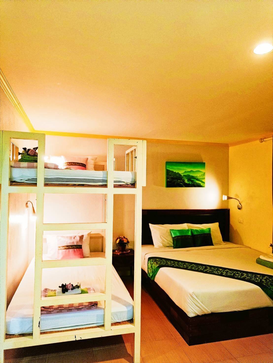 Una habitación con literas y una cama individual, un cuadro en la pared y una lámpara de noche.