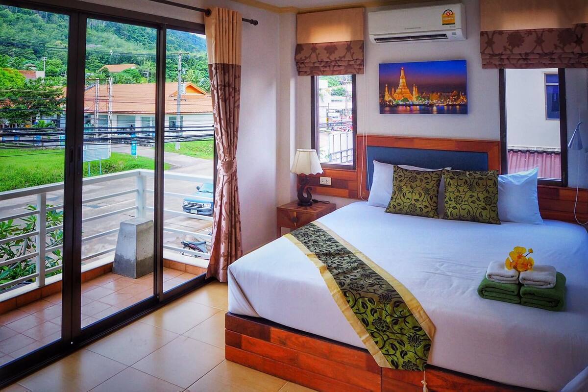 A hotel room with a large bed, a view of a cityscape, and a balcony with a view of the city and greenery.