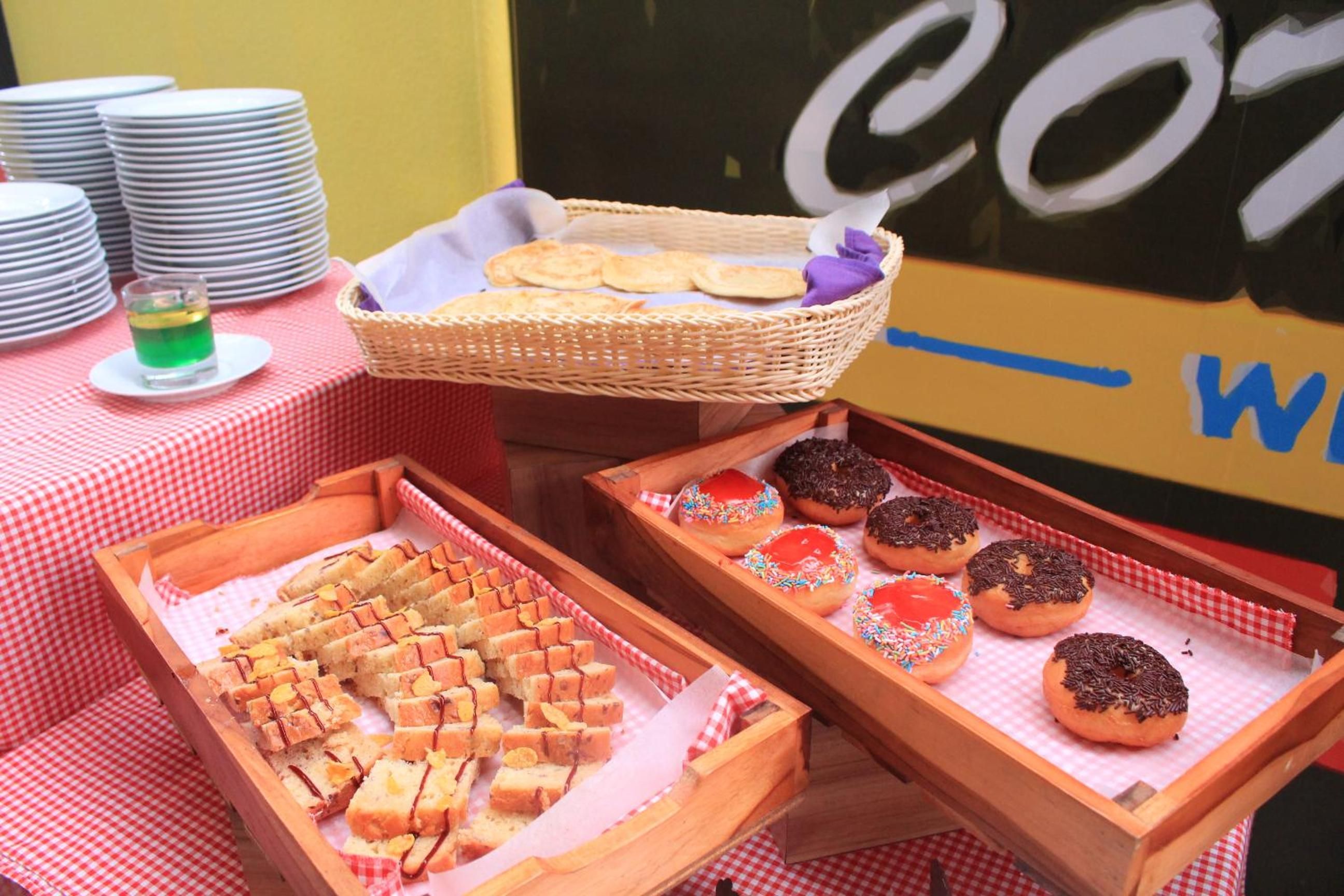 A table with trays of food, including bread and donuts, and a stack of plates.
