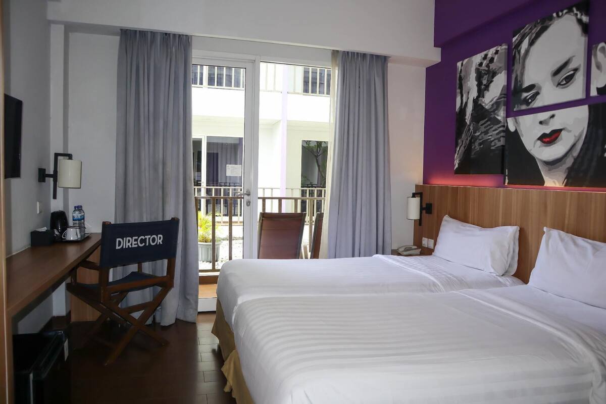 A hotel room with a bed, a desk, a chair labeled 'DIRECTOR', and a large window with curtains.