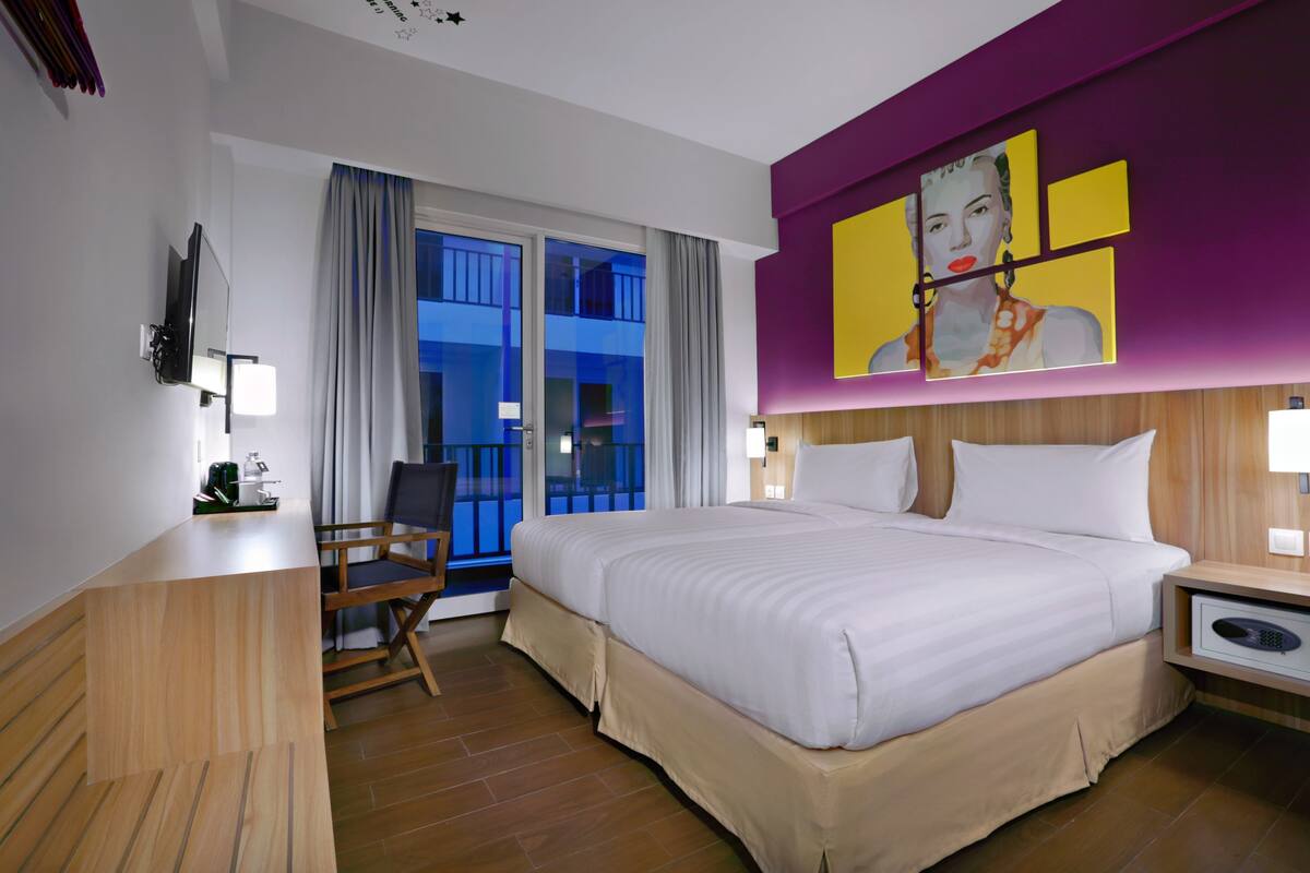A hotel room with a large bed, a desk, a chair, a TV, and a painting on the wall.
