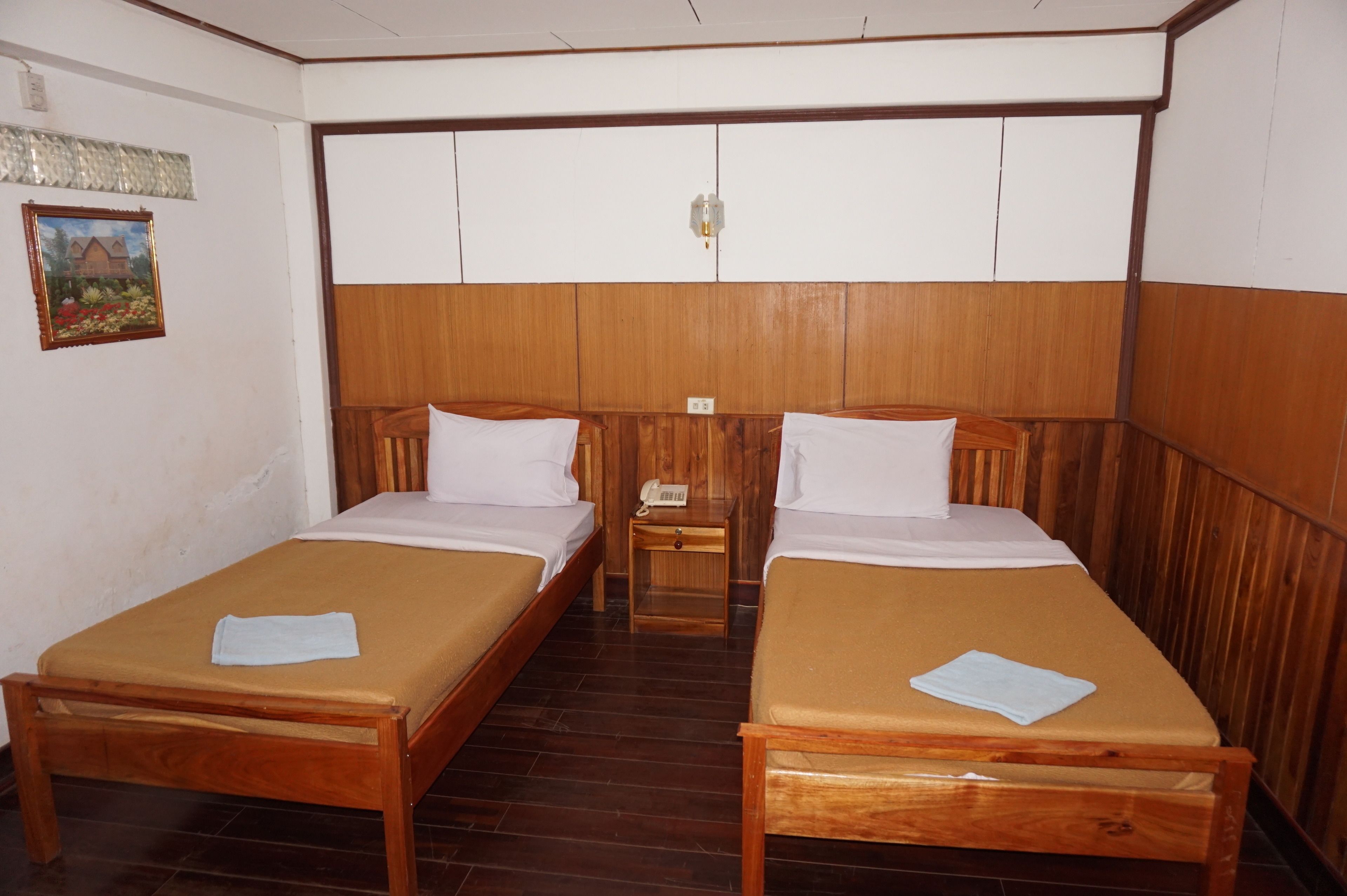 A room with two wooden beds, a small wooden table, and a wall-mounted telephone.
