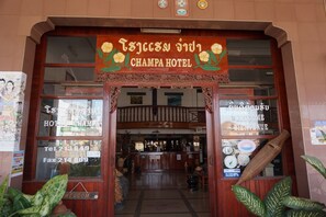 La entrada del Hotel Champa, con fachada de madera, un mostrador de recepción y un cartel con el nombre del hotel.