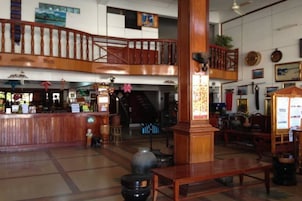 A spacious lobby with a wooden reception desk, a staircase, and a seating area.