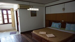 A room with a wooden bed, a window with curtains, an air conditioning unit, and a small painting on the wall. - Champa Hotel (Pakse)