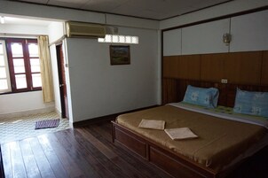 A room with a wooden bed, a window with curtains, an air conditioning unit, and a small painting on the wall.