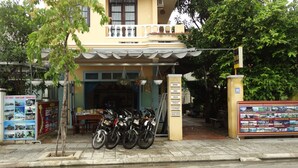 A building with a balcony, a signboard listing amenities like room, bike, tour, ticket, laundry, and free info. - Yellow House Homestay (Da Nang)