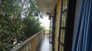 A covered balcony with a tiled floor, a balustrade, and a view of a building with a glass door. - Yellow House Homestay (Da Nang)