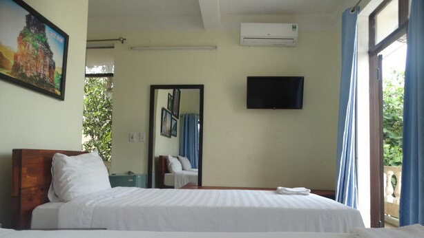 A hotel room with a bed, a flat-screen TV, an air conditioner, and a window with curtains. - Yellow House Homestay (Da Nang)