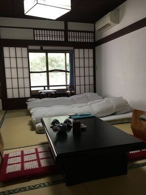 A traditional Japanese-style room with tatami flooring, a low table with a tea set, and a futon bed. - Ryoso Kawaguchi (Hatsukaichi)
