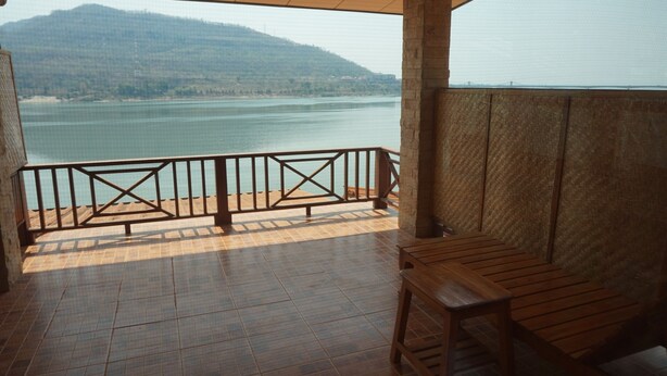 A balcony with a view of a lake and mountains, featuring a wooden table and a metal railing. - Mekong Paradise Resort (Pakse)