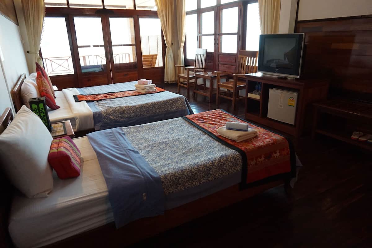 A room with two beds, a TV, a desk, and a window with curtains.