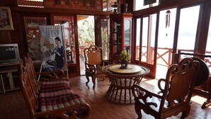 A wooden-floored room with a round table, chairs, a sofa, and a fan. - Mekong Paradise Resort (Pakse)