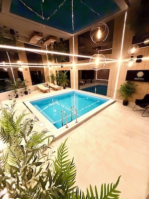 Une piscine intérieure à l’eau claire, entourée de chaises longues et de plantes en pot.
