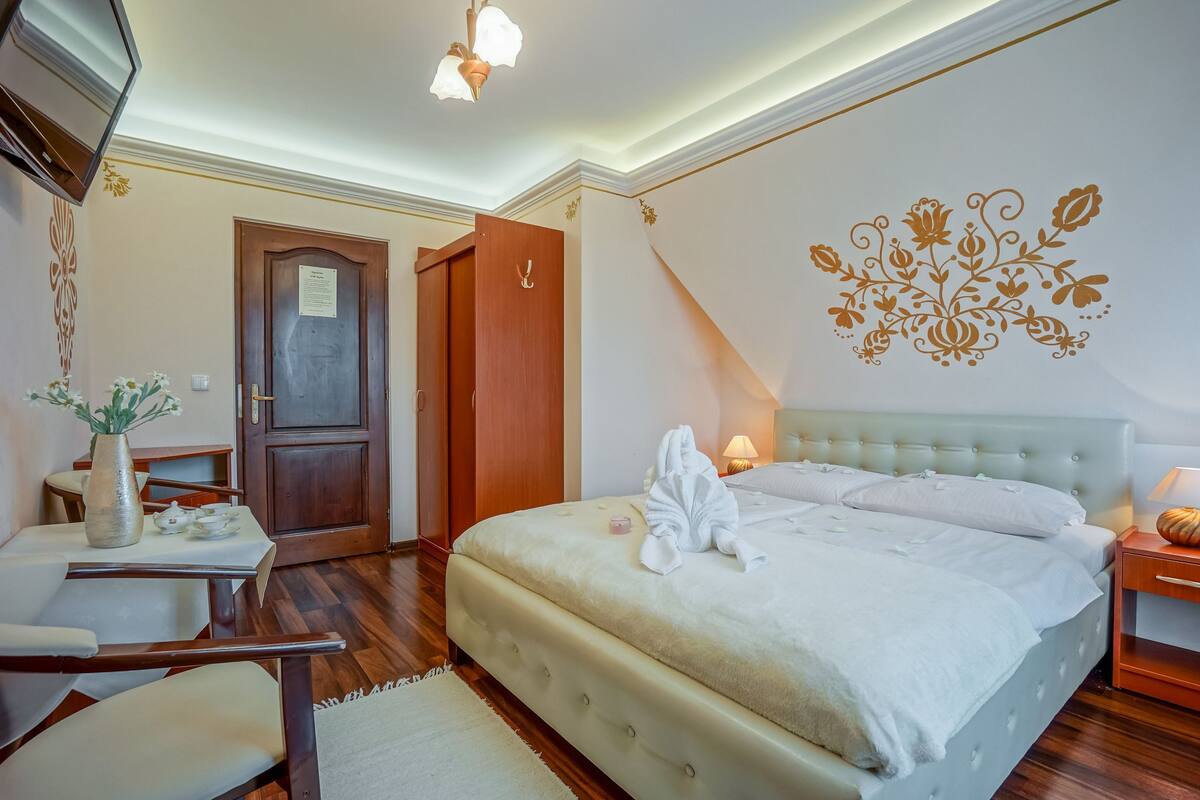 A hotel room with a bed, bedside tables, a desk, a chair, a vase with flowers, and a decorative wall.