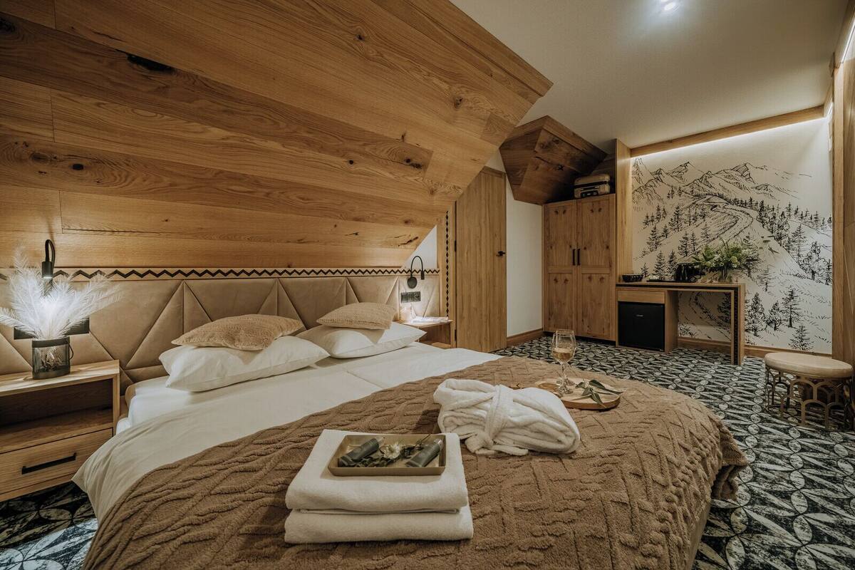 A bedroom with a large bed, wooden headboard, a nightstand, a bedside table, a dresser, and a wall with a mountain design.