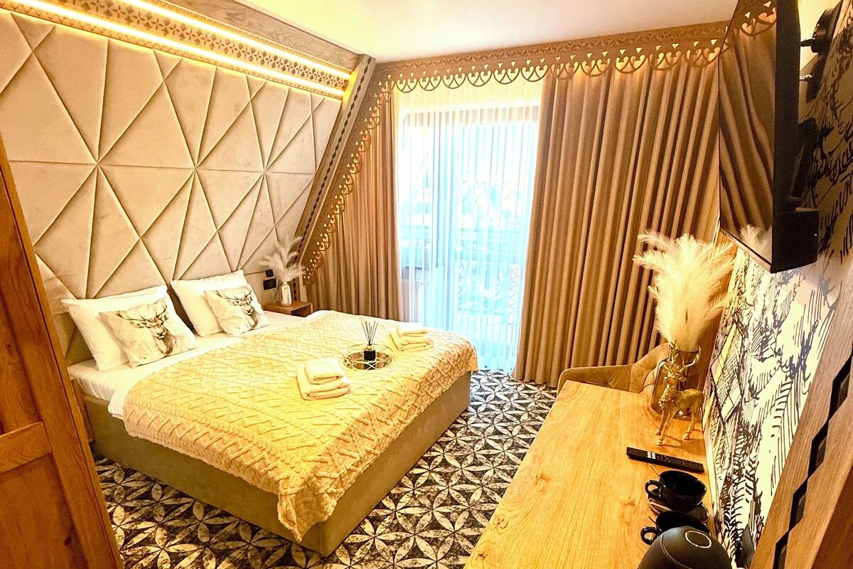 A hotel room with a large bed, a wooden desk, and a television on the wall.