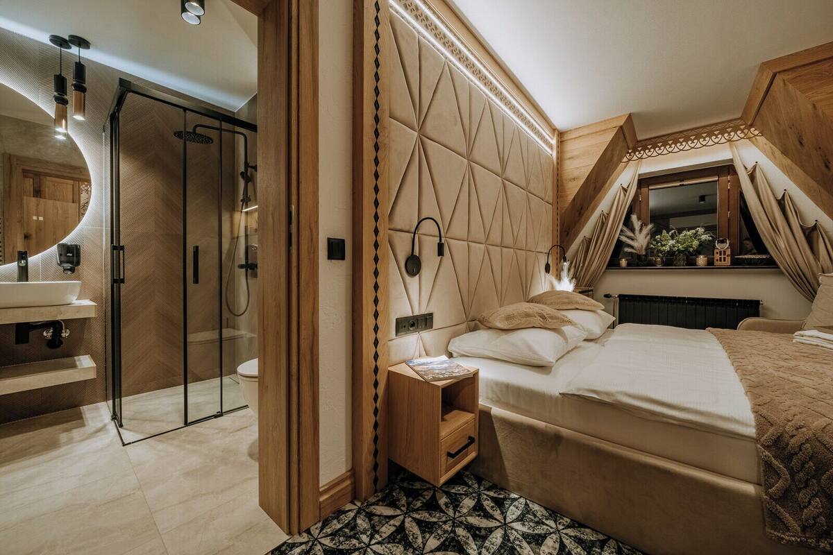 A modern bedroom with a glass shower, a wooden vanity, a bedside table, and a bed with a headboard.