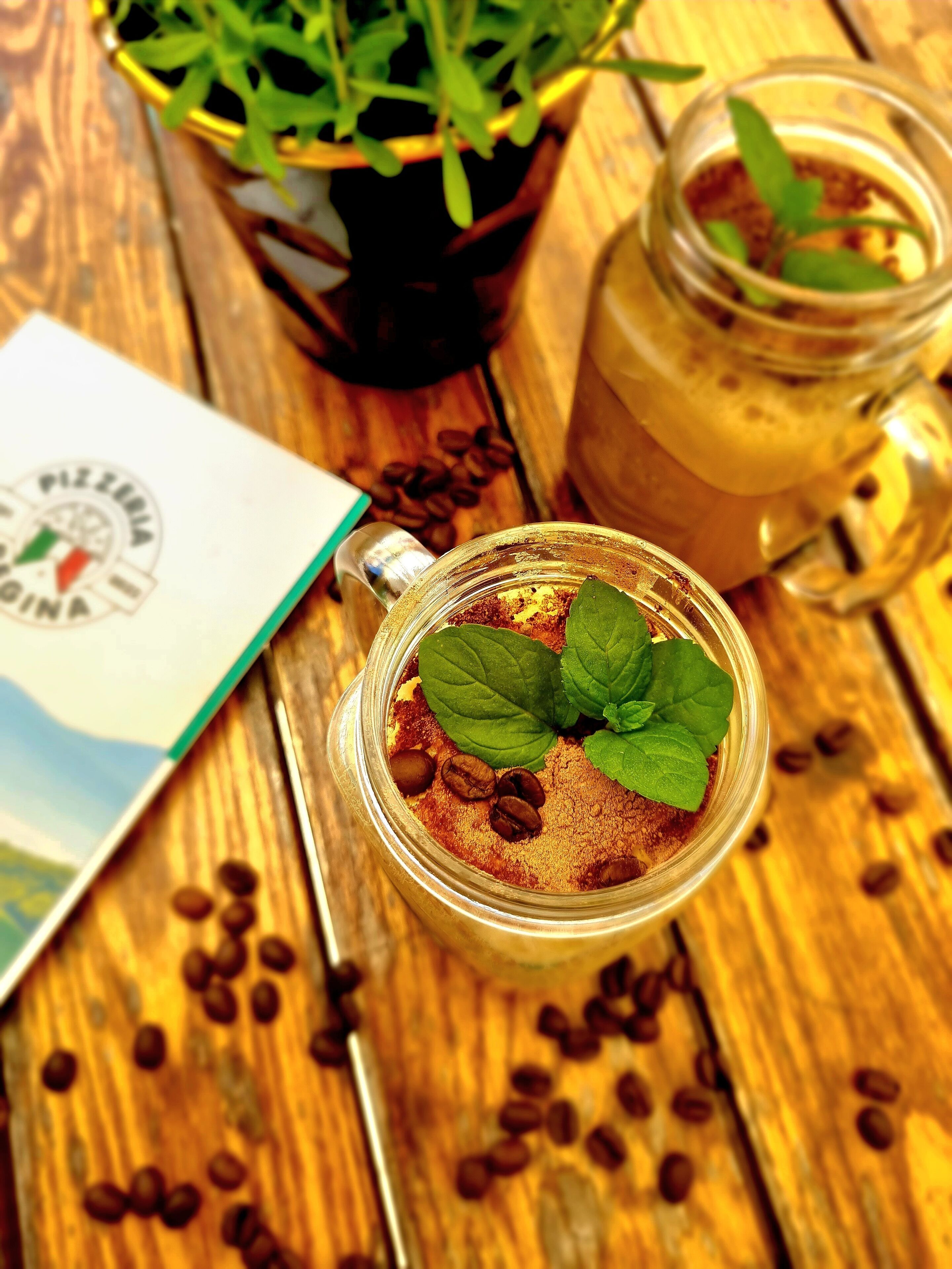 A glass jar with a spoon, surrounded by coffee beans on a wooden surface.