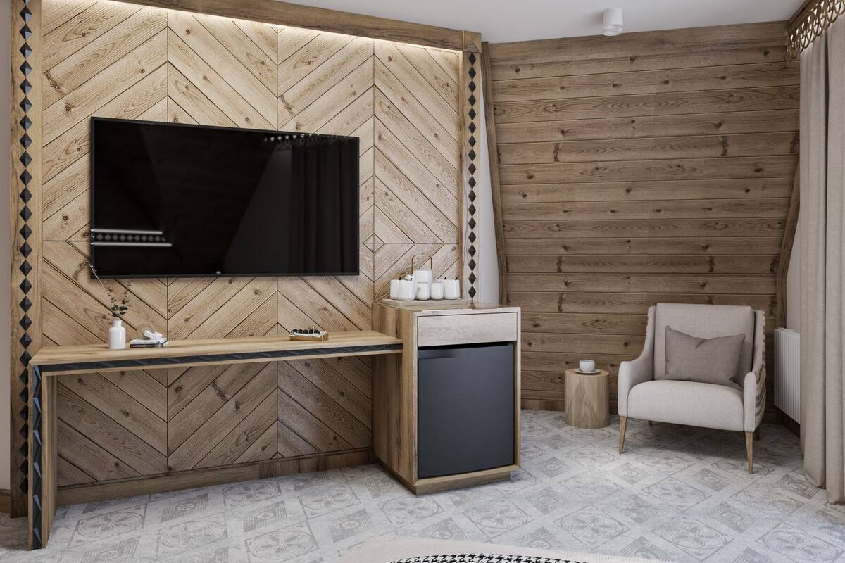 A modern room with a herringbone wood wall, a flat-screen TV, a wooden desk, a chair, and a small side table.
