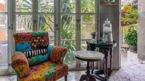 Una habitación con un sillón colorido, una mesita redonda y vistas a zonas verdes a través de amplios ventanales.