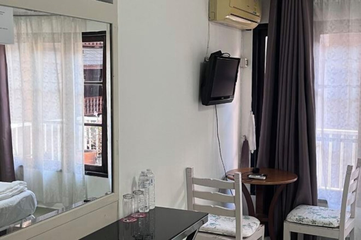 Une chambre d’hôtel avec un lit, une petite table avec des chaises, un téléviseur fixé au mur et une fenêtre avec des rideaux.
