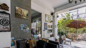 Una sala de estar acogedora con un sofá negro, una mesita de centro y una estantería llena de libros. Se aprecia una ventana grande con vistas al exterior, y una planta en maceta en el alféizar.