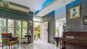 Un salón amplio con suelo de mármol, un piano, cojines de colores y ventanas grandes que ofrecen vistas al exterior.