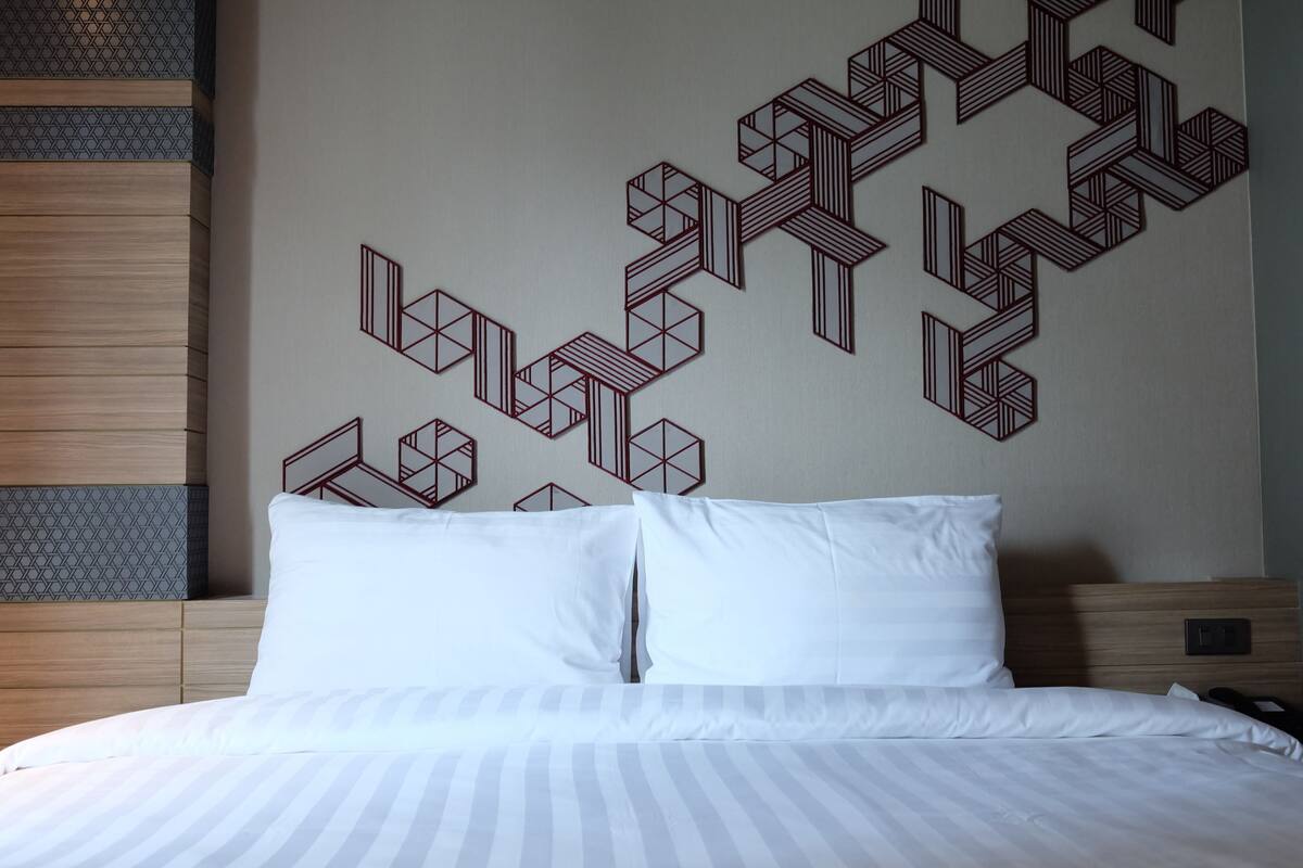A hotel room with a bed, white pillows, and a geometric wall design.