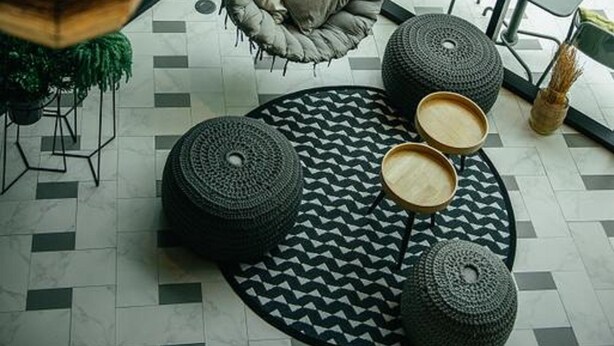 Ein moderner Außenbereich mit Hängestühlen, runden Poufs und einem gemusterten Teppich.