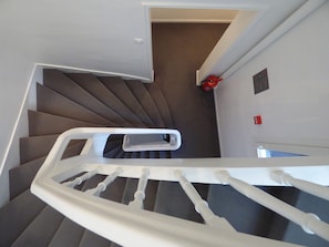 A spiral staircase with a white handrail, carpeted steps, and a red fire extinguisher on the wall. - Rive Gauche (Saumur)
