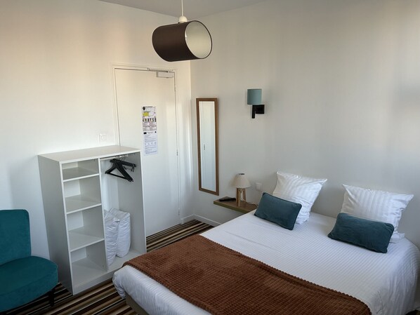Une chambre d’hôtel comprenant un lit, une armoire, un bureau, une chaise, un miroir et une lampe.