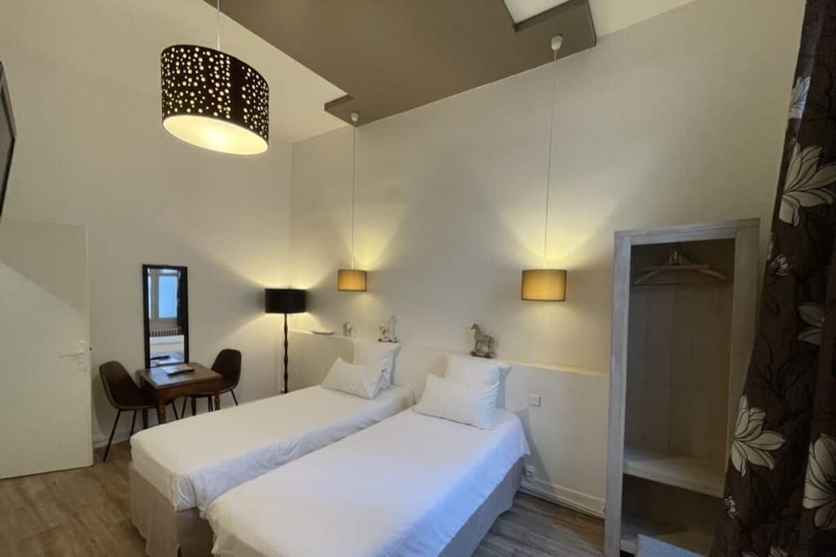 Ett hotellrum med två sängar, ett skrivbord, en stol, en garderob och en hängande lampa.