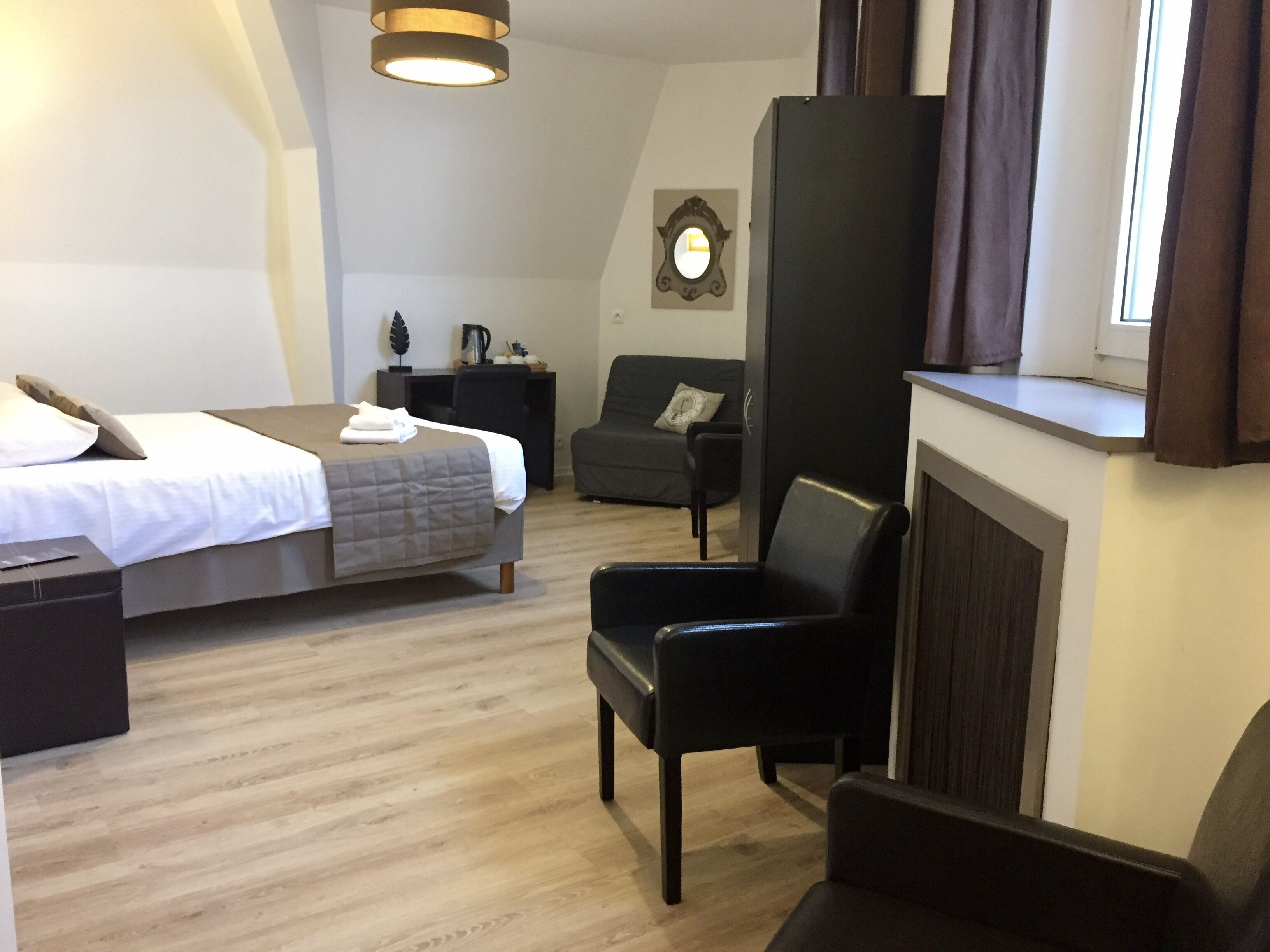 Habitación de hotel con cama, escritorio, silla, un reloj en la pared y una ventana con cortinas.