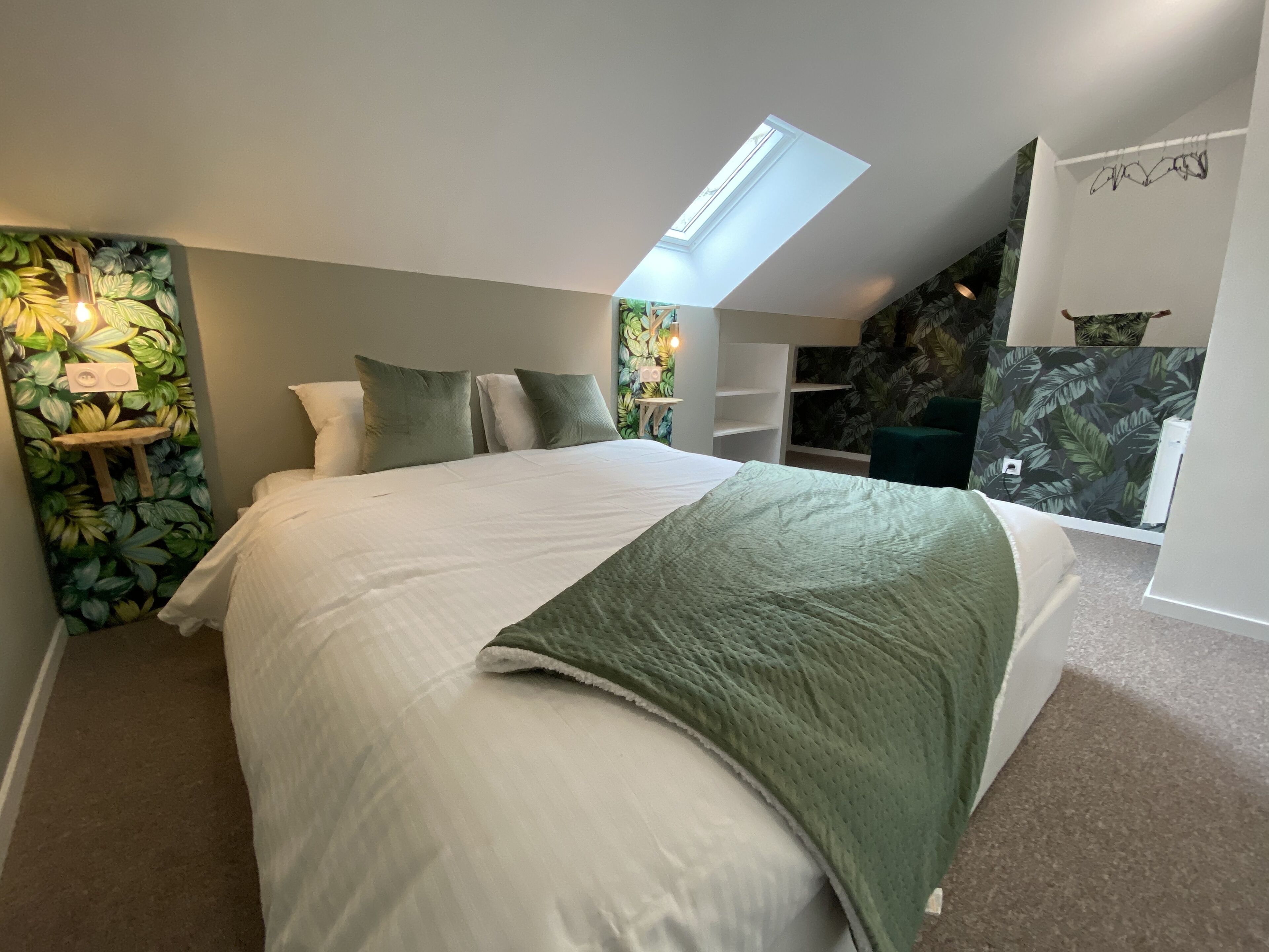Quarto com claraboia, cama com manta verde e parede com padrão de folhas.