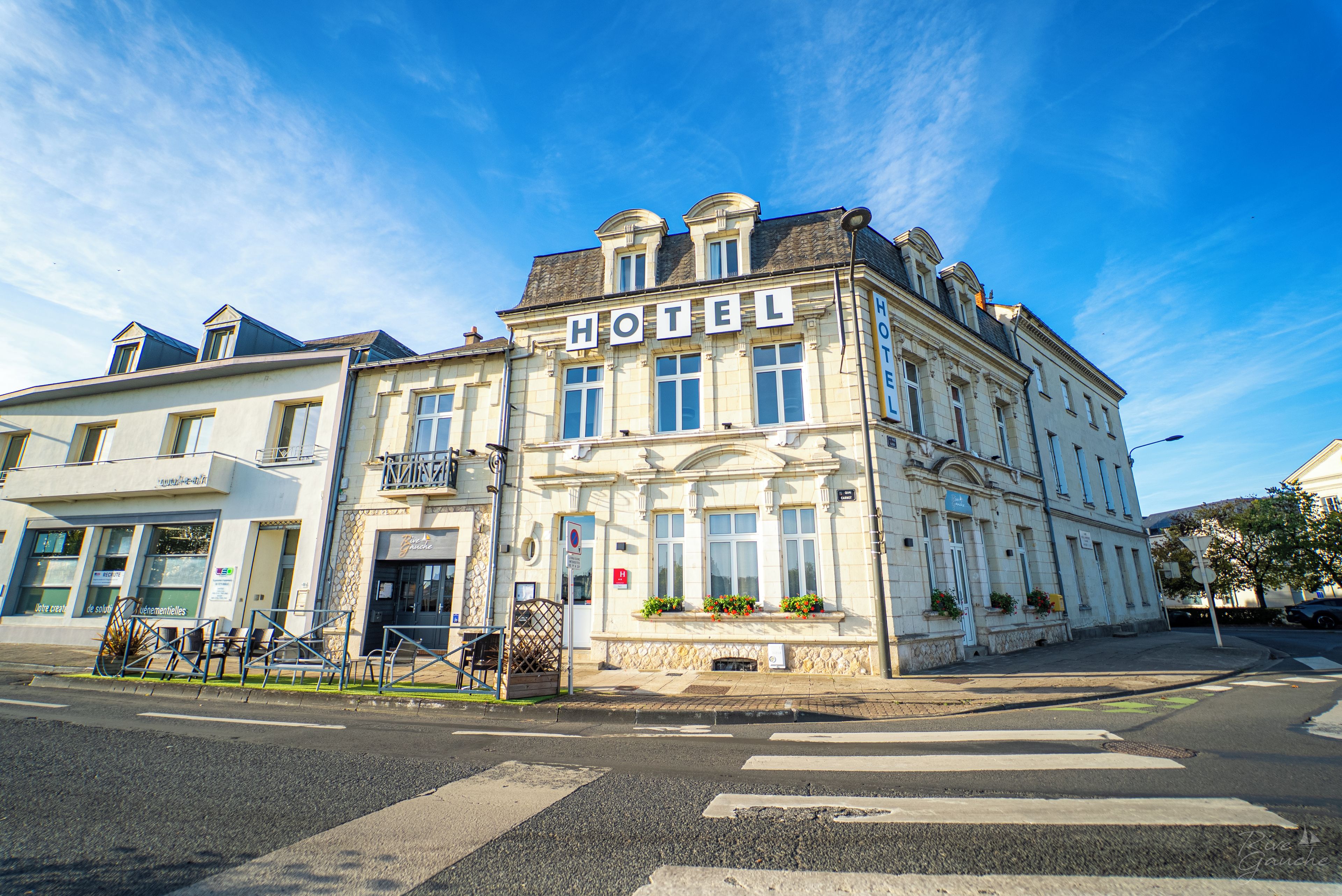 Un bâtiment historique, reconnaissable à son grand panneau « HÔTEL », à ses larges fenêtres et à son emplacement en angle, à la croisée de deux rues.