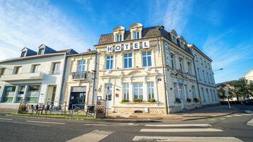 Un bâtiment historique, reconnaissable à son grand panneau « HÔTEL », à ses larges fenêtres et à son emplacement en angle, à la croisée de deux rues.