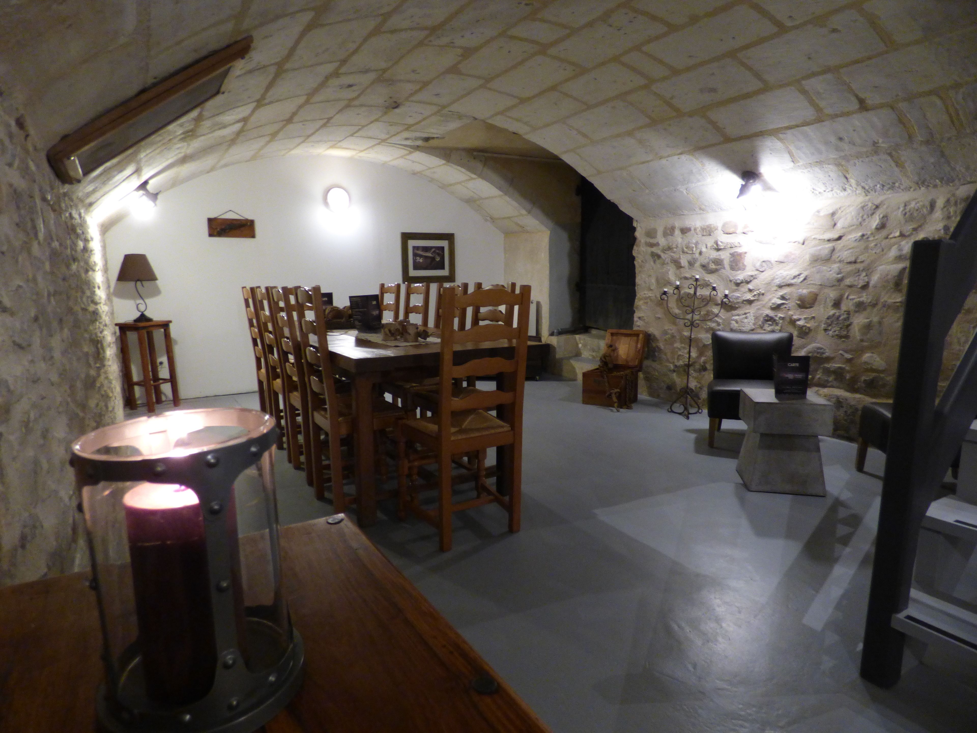 A dining area with a stone wall, wooden chairs, a table, and a candelabra.