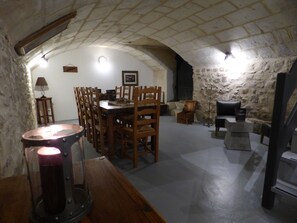 A dining area with a stone wall, wooden chairs, a table, and a candelabra. - Rive Gauche (Saumur)