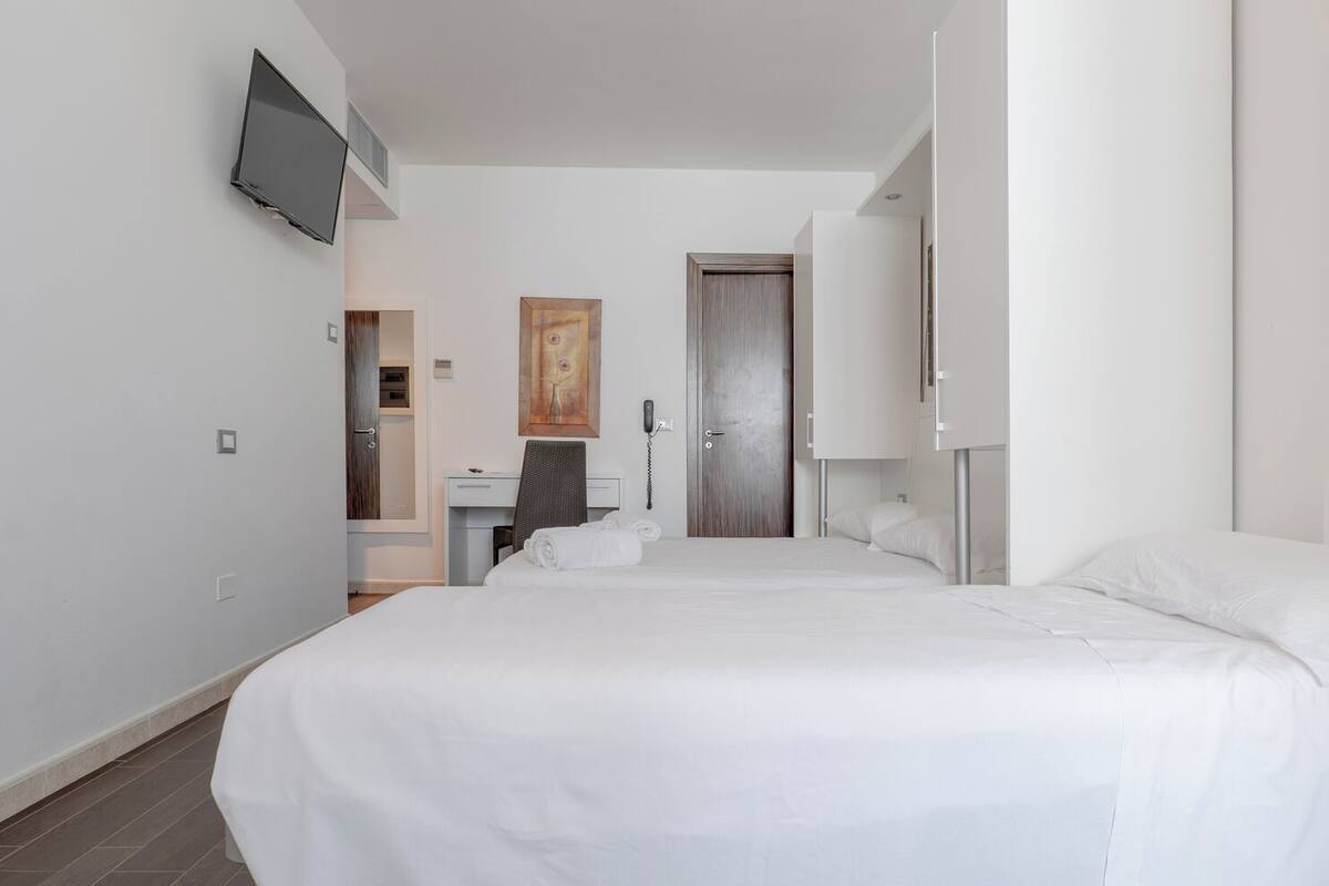 A hotel room with a large bed, a desk, a chair, a telephone, and a painting on the wall.