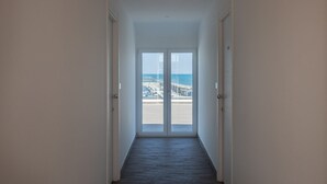 A hallway leading to a glass door with a view of a beach and marina. - Nauticus Hotel Ugento (Ugento)