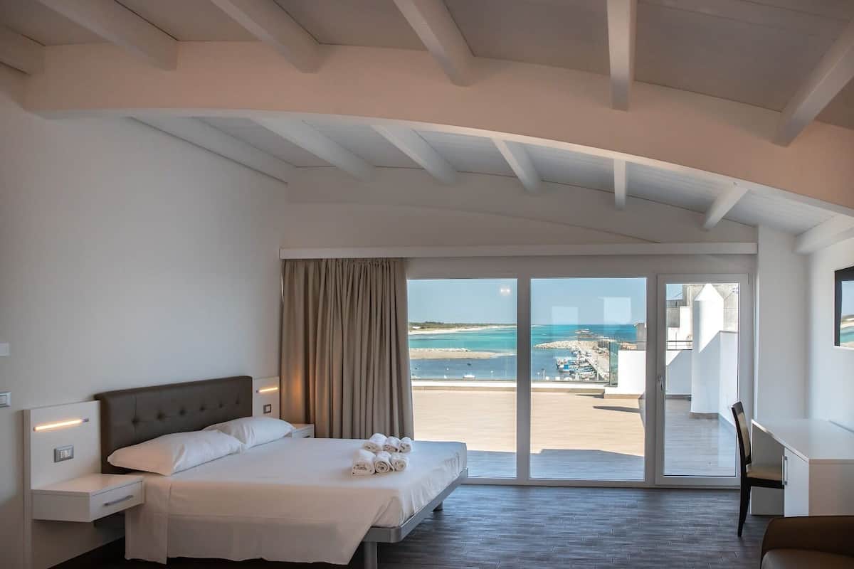 A hotel room with a bed, a desk, and a view of the sea.