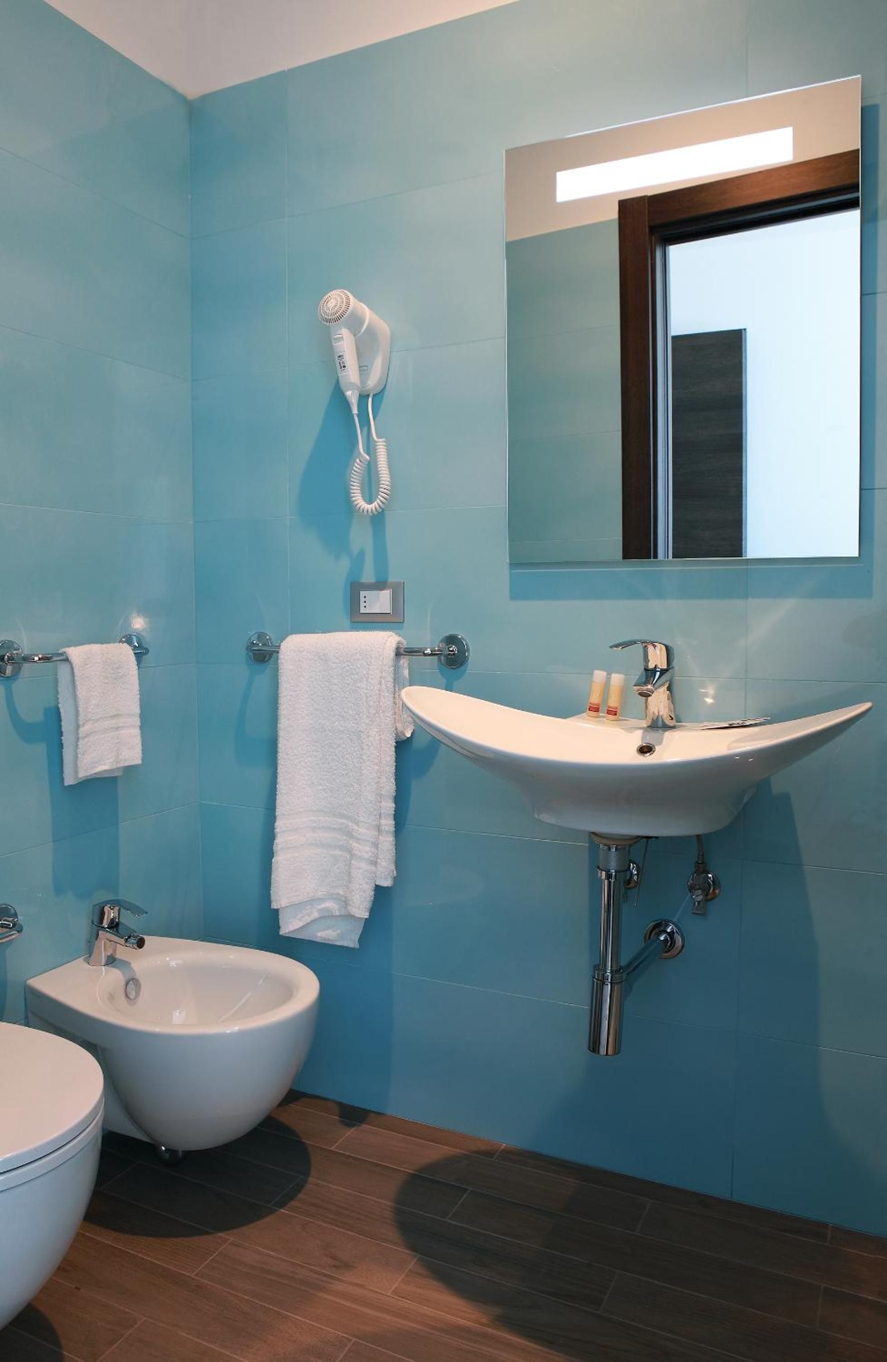 A bathroom with a bidet, a sink, a mirror, and a hairdryer mounted on the wall.