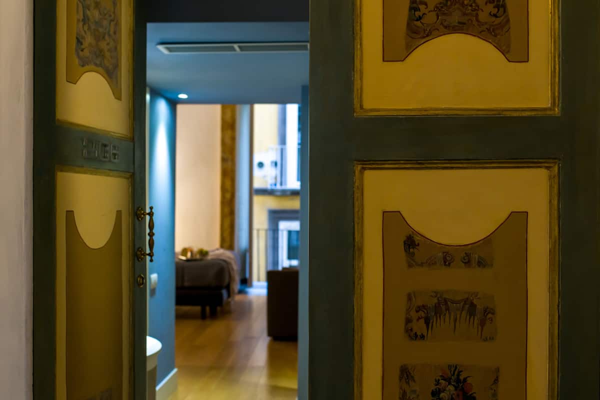 Un couloir avec une porte portant l’inscription « 216 », qui donne sur une pièce contenant un lit et une table.