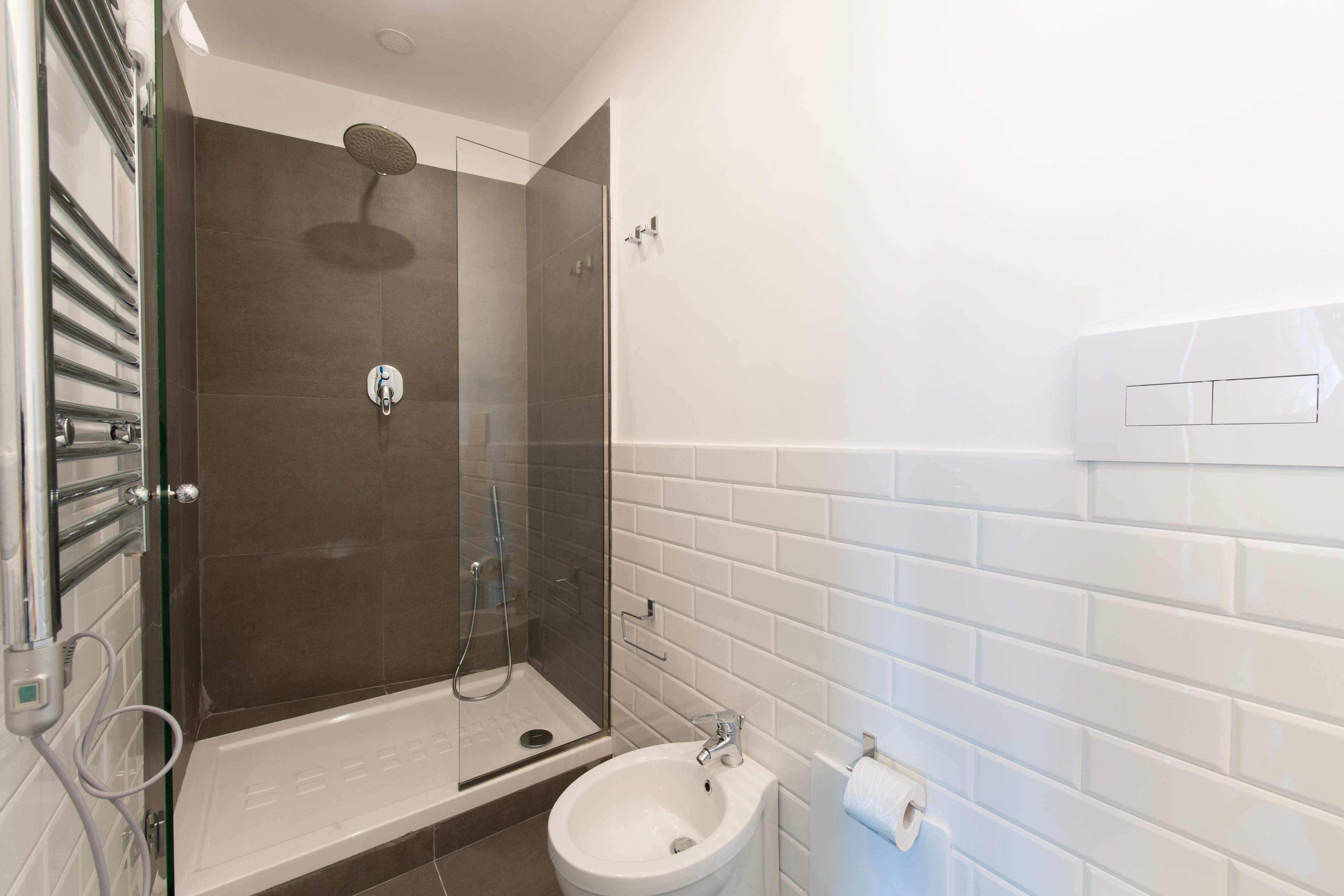 A modern bathroom with a glass-enclosed shower, a white sink, and a white tiled wall.