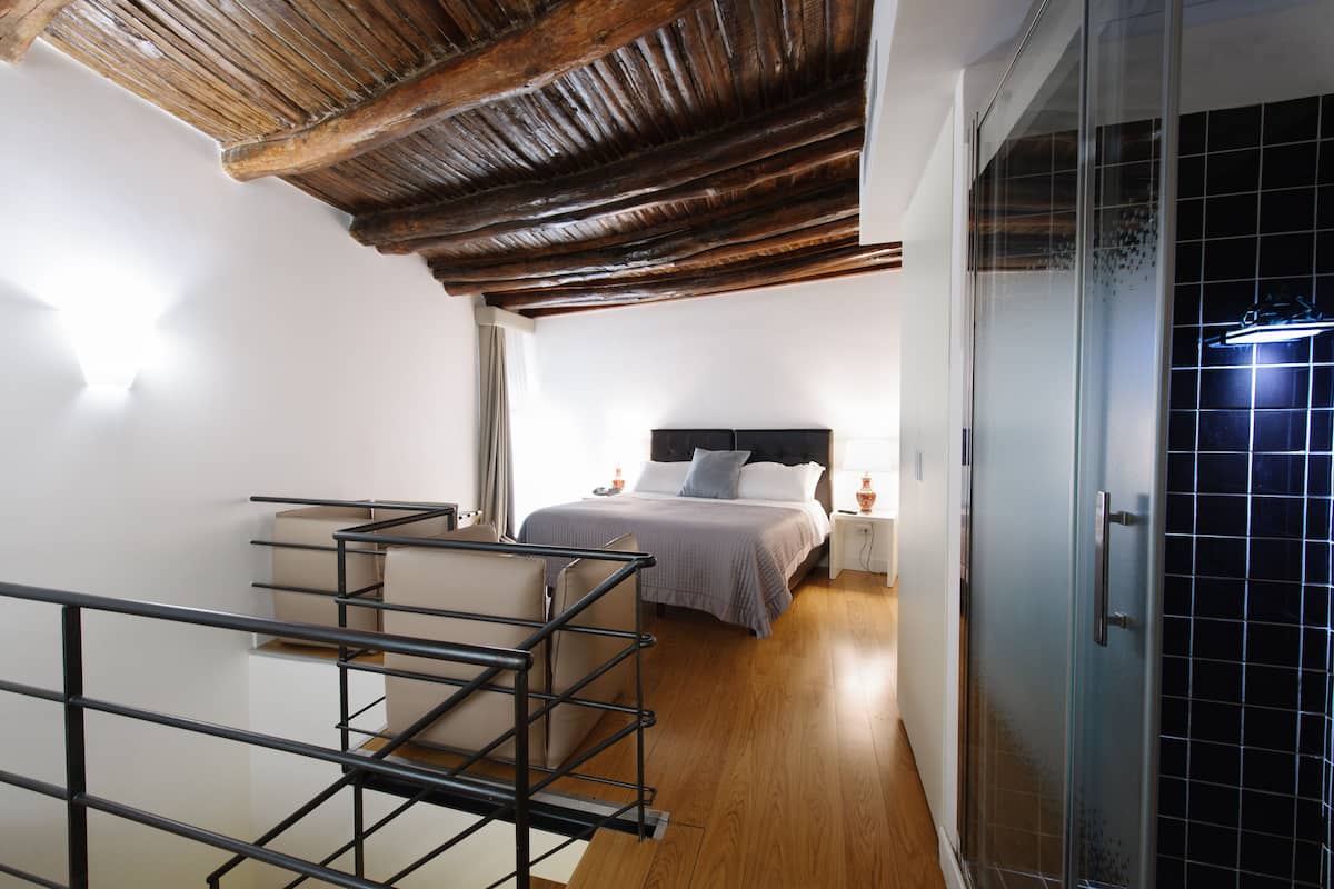 Une chambre avec un plafond en bois, un lit avec une tête de lit, une table de chevet et une cabine de douche en verre.