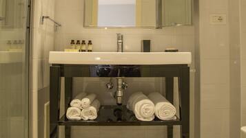 A bathroom with a glass shower enclosure, a white sink with a dark countertop, a mirror above the sink, and a tiled floor with a geometric pattern.